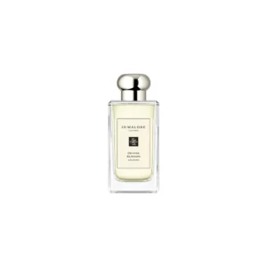 Przejrzysty flakon Jo Malone Orange Blossom 100 ml na tle kwitnącego, słonecznego ogrodu cytrusowego.