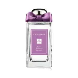Elegancki flakon Jo Malone Plum Blossom 100 ml otoczony białymi i różowymi płatkami kwitnących drzew.