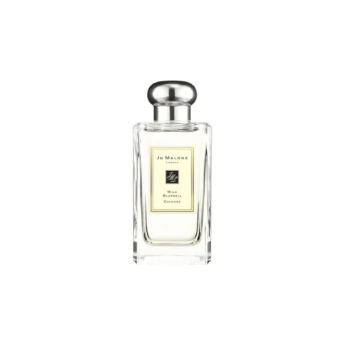 Jo_Malone_Wild_Bluebell_2 Przejrzysty flakon Jo Malone Wild Bluebell na tle polnych, niebieskich kwiatów w lesie.